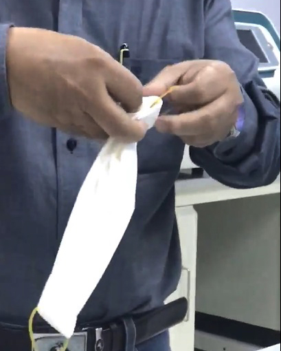 Bước 2: Thắt 4 sợi thun làm 2 phần, sau đó dùng bấm giấy kẹp giữ vào hai đầu khăn giấy đã xếp trước đó để làm dụng cụ đeo, ảnh cắt từ clip